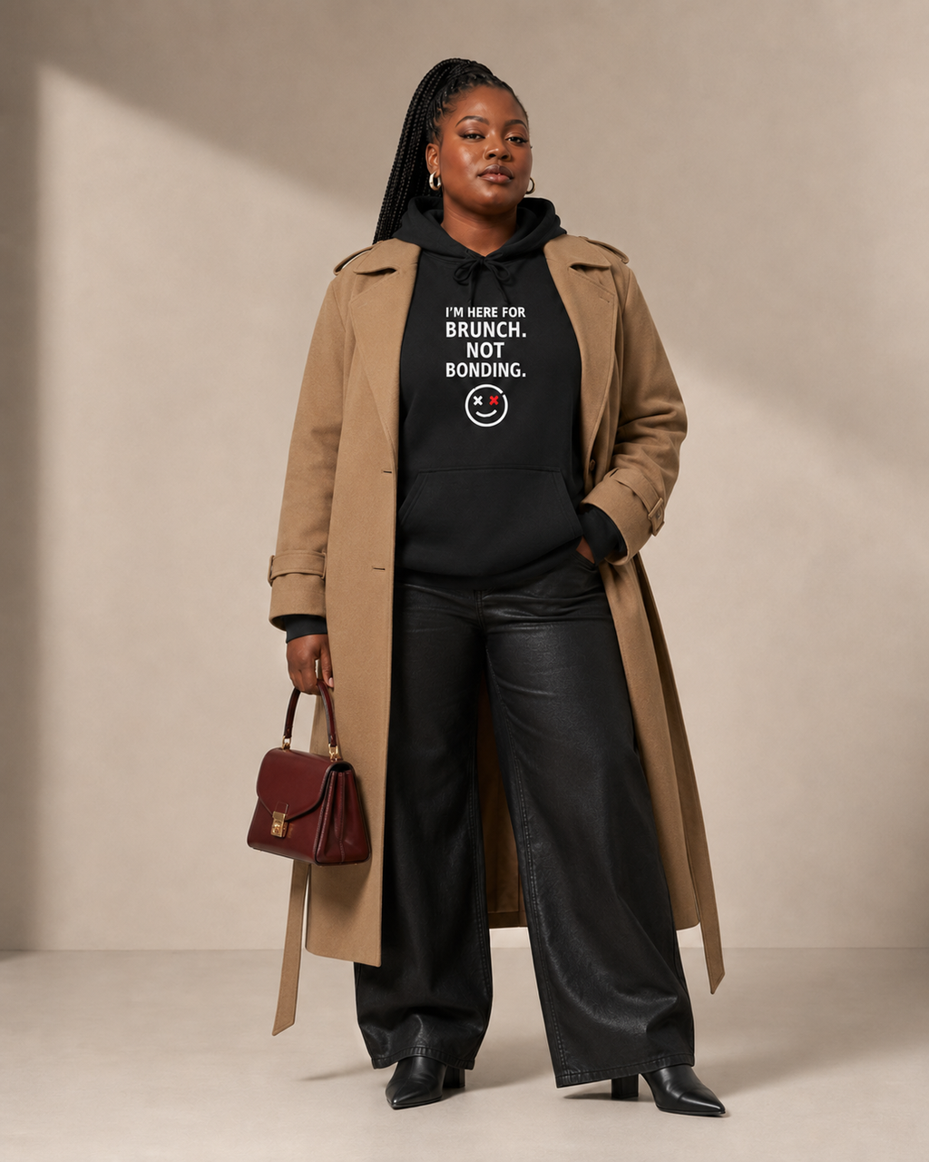 Plus-size Black woman styling the I'm Here for Brunch. Not Bonding. black hoodie with an open camel trench coat, black wide-leg pants, boots, and burgundy handbag